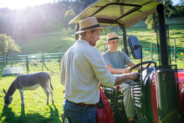 Farmer father letting his son drive the tractor. Young boy growing up and working on family farm. Concept of multigenerational farming.