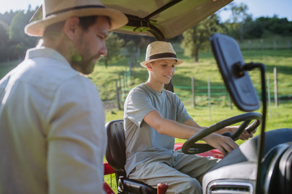 Farmer father letting his son drive the tractor. Young boy growing up and working on family farm. Concept of multigenerational farming.