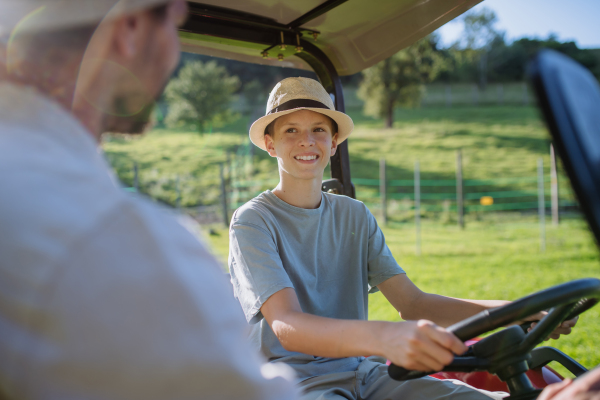 Farmer father letting his son drive the tractor. Young boy growing up and working on family farm. Concept of multigenerational farming.