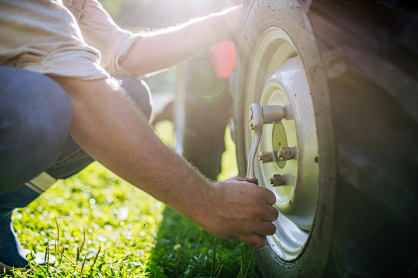 Farmer fixing wheel on tractor. Tractor maintenance. Harvesting crops, collecting vegetables on family farm. Concept of farming and agricultural business. Close up.