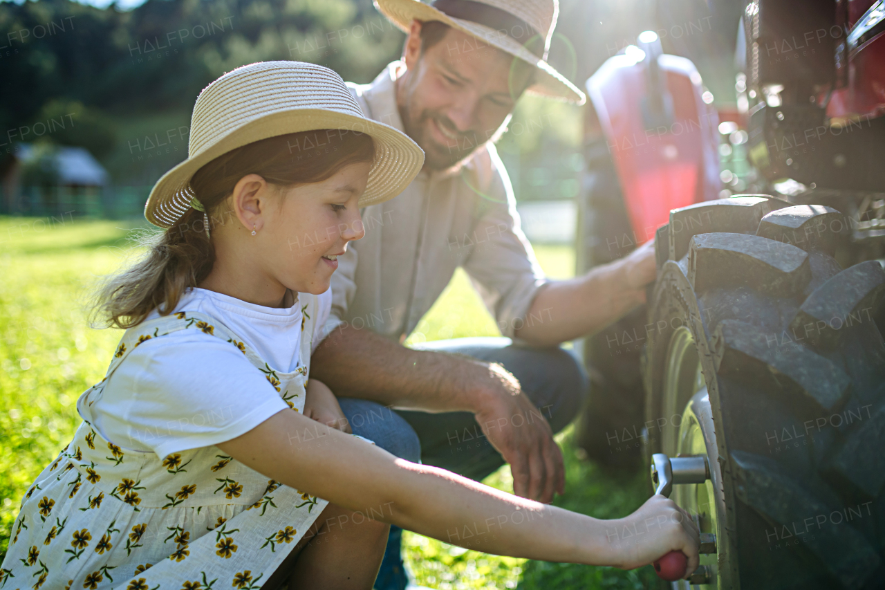 Farmer father teaching daughter how to fix a wheel on a tractor. Young girl growing up and working on family farm. Concept of women in agriculture.