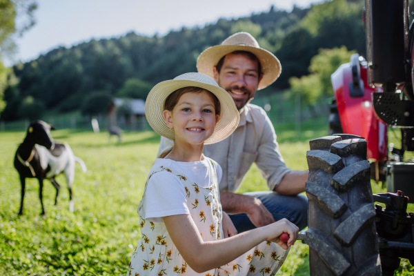 Farmer father teaching daughter how to fix a wheel on a tractor. Young girl growing up and working on family farm. Concept of women in agriculture.