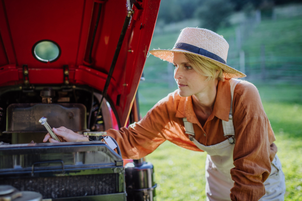 Female farmer fixing tractor, a tractor maintenance.Progressive female farmer working on tractor on her own farm. Women in agriculture.