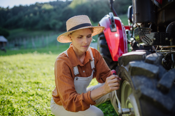 Female farmer fixing a wheel on a tractor. Progressive female farmer working on tractor on her own farm. Women in agriculture.