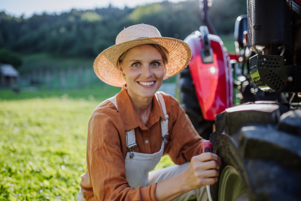 Female farmer fixing a wheel on a tractor. Progressive female farmer working on tractor on her own farm. Women in agriculture.