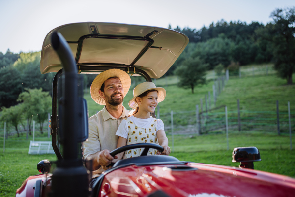 Farmer father riding tractor with his daughter. Young girl growing up on family farm. Concept of multigenerational farming.