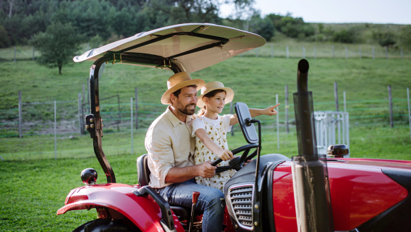 Farmer father riding tractor with his daughter. Young girl growing up on family farm. Concept of multigenerational farming.