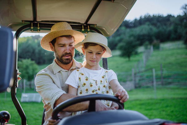 Farmer father riding tractor with his daughter. Young girl growing up on family farm. Concept of multigenerational farming.