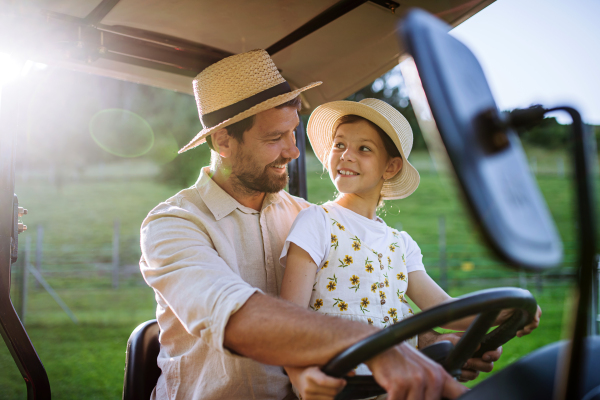 Farmer father riding tractor with his daughter. Young girl growing up on family farm. Concept of multigenerational farming.