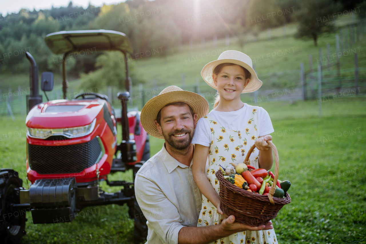 Portrait of farmer father with daughter holding harvest basket full of fresh vegetables. Harvesting crops, collecting vegetables on family farm. Concept of multigenerational farming.