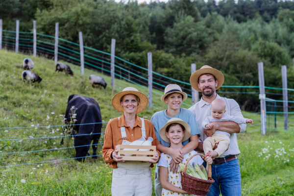 Portrait of farmer family holding harvest basket full of fresh vegetables, in front of paddock. Concept of multigenerational and family farming.