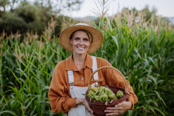 Portrait of female farmer holding basket full of harvested corn. Concept of multigenerational and family farming.