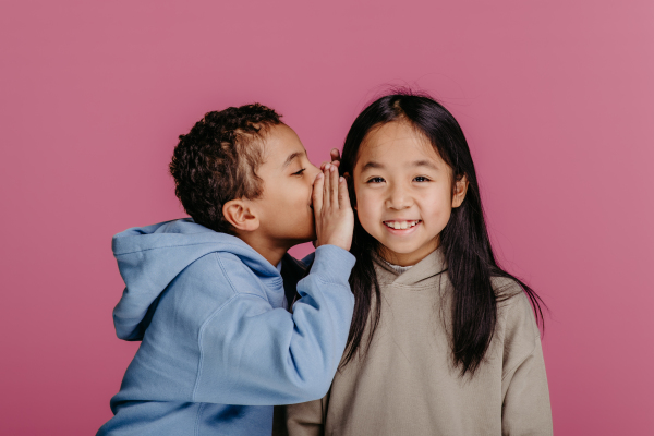 Portrait of little boy whispering something to girl standing next to him.