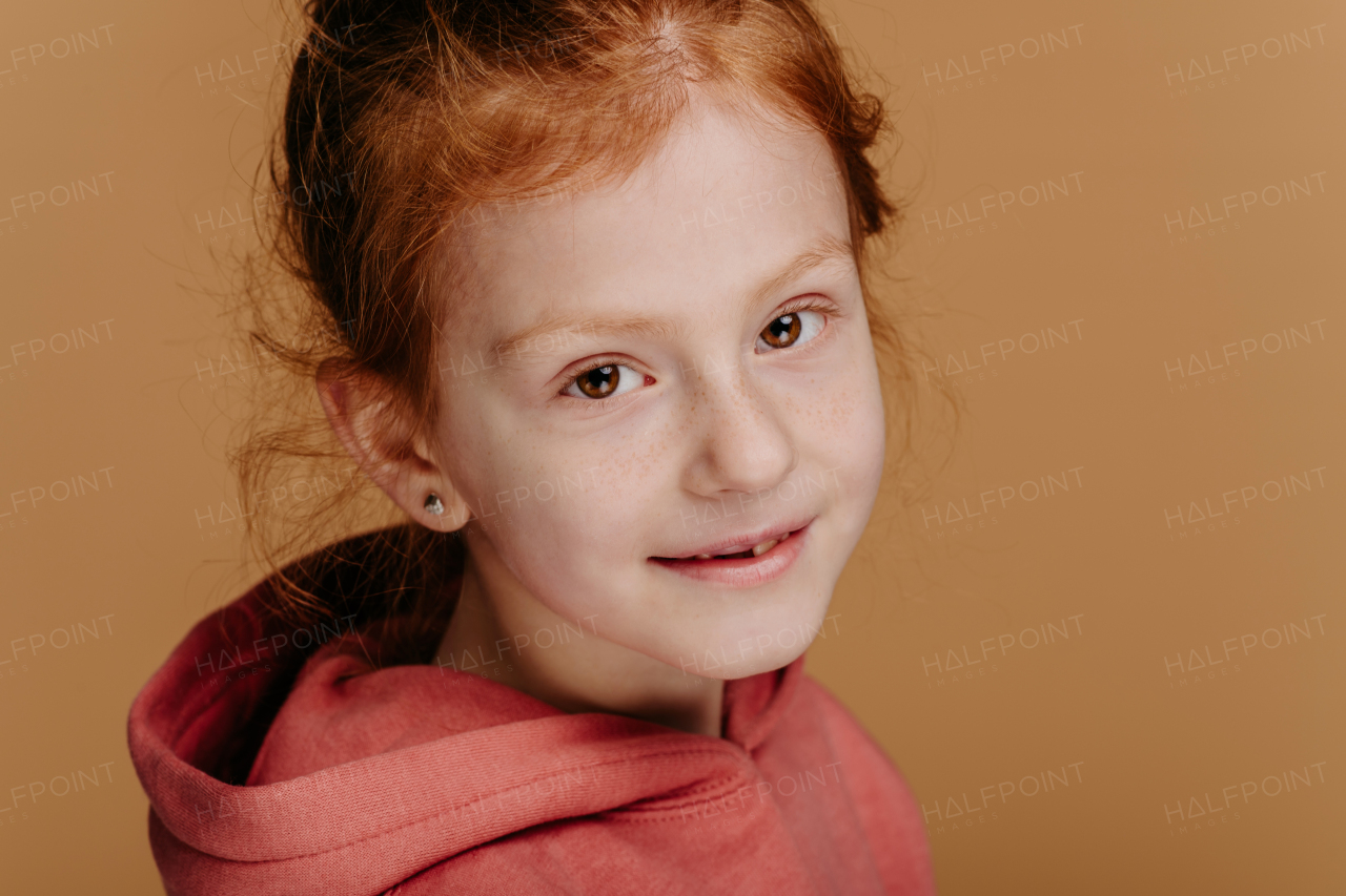 Portrait of little redhead girl in hoodie, studio shoot.