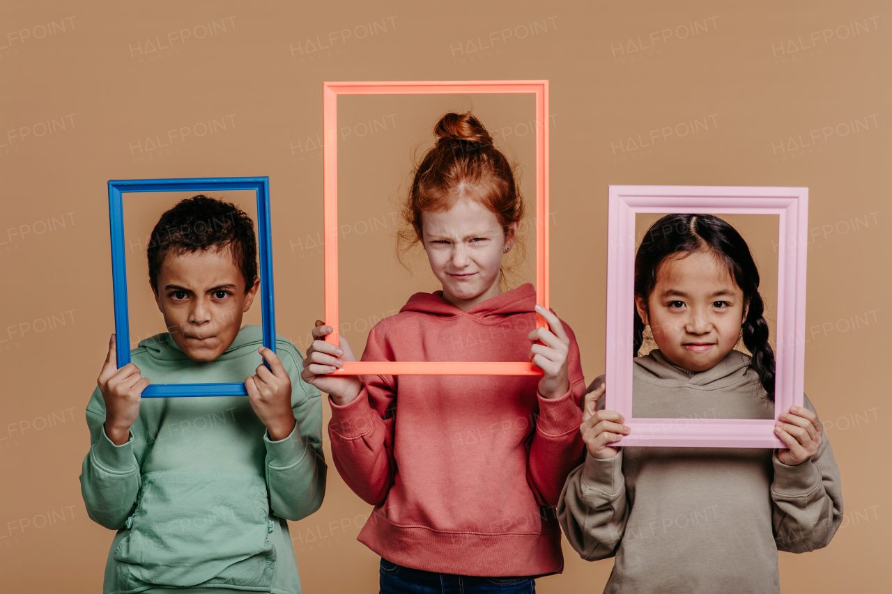 Portrait of three children with frames, studio shoot. Concept of diversity in a friendship.