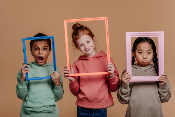 Portrait of three children with frames, studio shoot. Concept of diversity in a friendship.