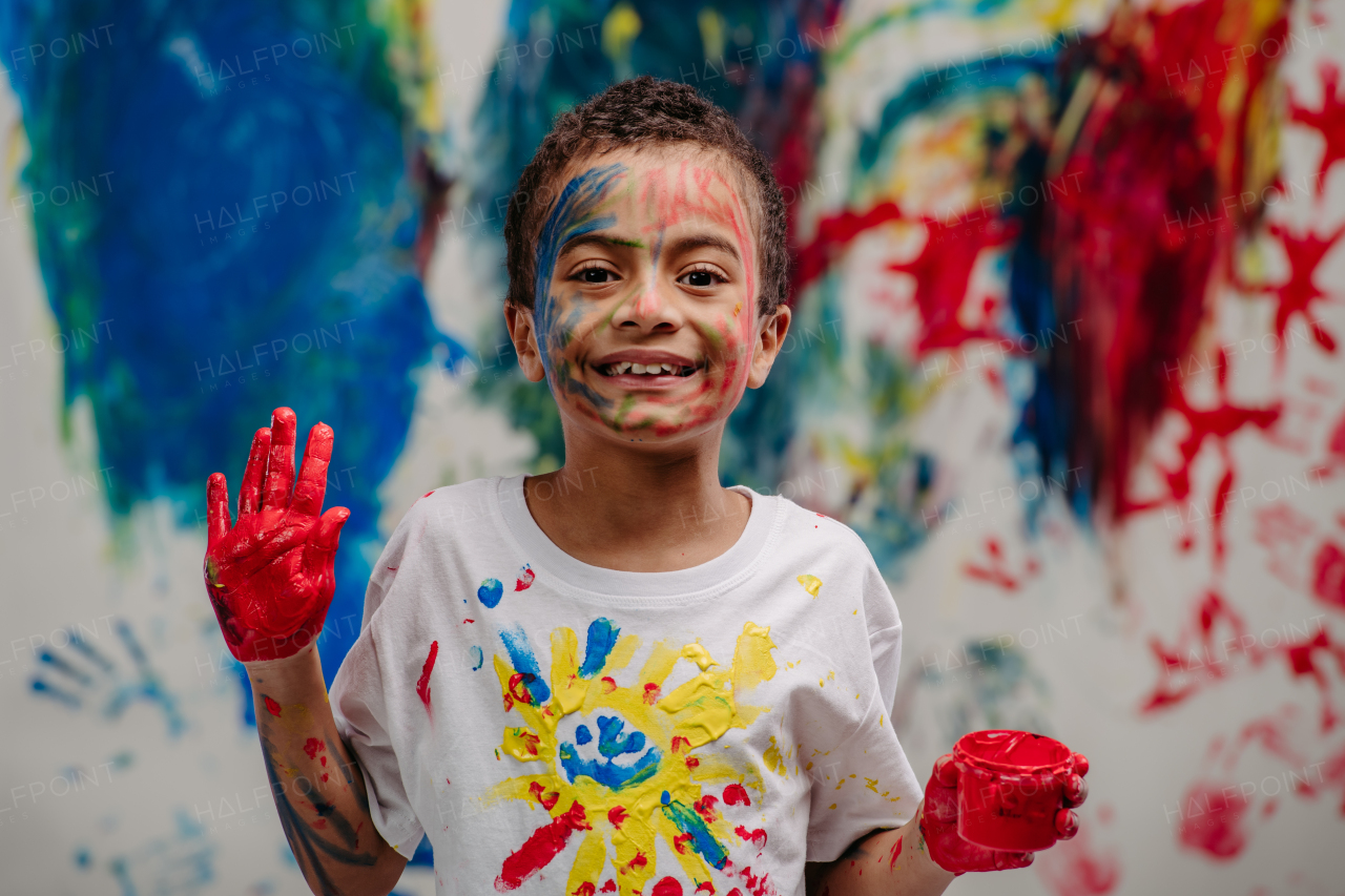 Portrait of happy boy with finger colours, painted t-shirt and background, studio shoot.