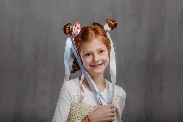 Portrait of little redhead girl with ribbons in hair, studio shoot.