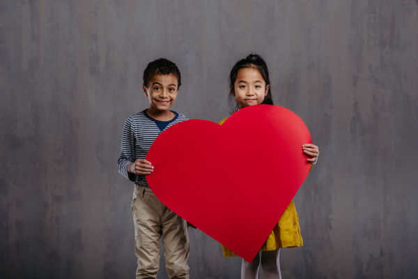 Studio shoot of little boy and girl holding paper heart.