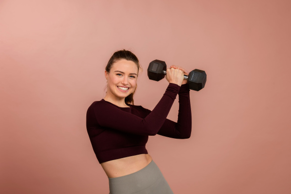 Portrait of young woman in sportive clothes with a dumbbell.