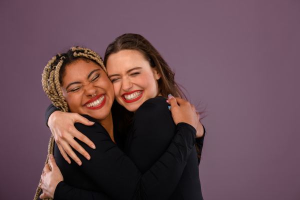 Two happy multiracial friends hugging and smiling.