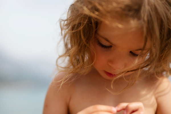 A summer outdoor close-up of little girl holding something in her hand and exploring it on holiday on beach.