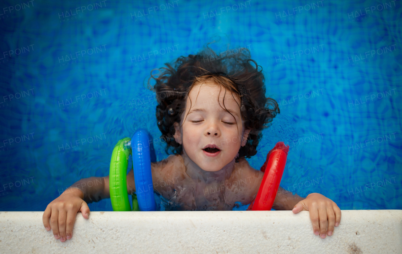 A top view of happy child wearing inflatable armbands learning to swim in swimming pool. Summer vacation concept.