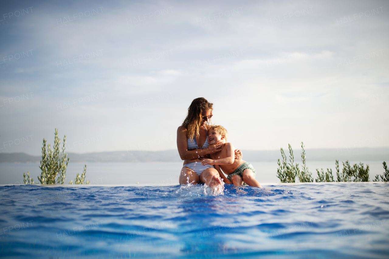 A happy family in the pool, having fun, mother with little son sitting on the edge of the pool and embracing. summer holidays vacation concept.