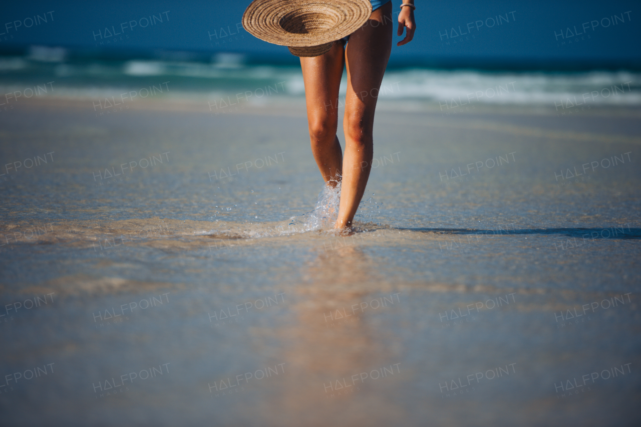 Close up of beautifuly shaped women's legs on the beach near the sea. Detail shot of woman on beach with straw hat in hand with copy space. Sandy beach and crystalline sea of Mnemba beach in Zanzibar. Concept of beach summer vacation.