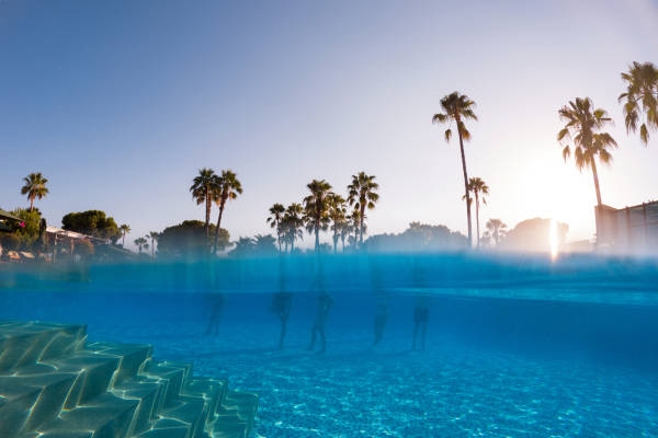 Underwater photography of people standing in the pool with copy space. Beach resort vacation by the sea. Winter or summer seaside resort holiday. Over-under underwater photography.