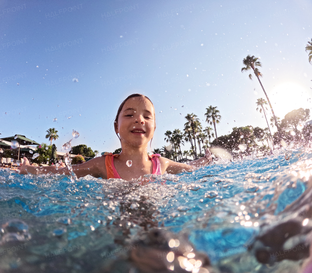 Little girl splashing water in the pool, playing in the water and having fun. Beach resort vacation by the sea. Winter or summer seaside holiday.