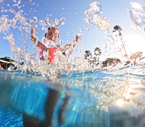 Little girl splashing water in the pool, playing in the water and having fun. Beach resort vacation by the sea. Winter or summer seaside holiday.