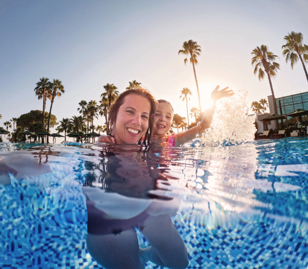 Mother teaching her daughter to swim in the pool during summer vacation. Mother and daughter playing in the water. Beach resort vacation by the sea. Winter or summer seaside holiday. Over-under underwater photograpy.