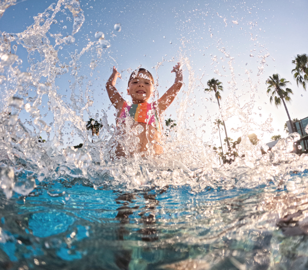 Little girl splashing water in the pool, playing in the water and having fun. Beach resort vacation by the sea. Winter or summer seaside holiday.