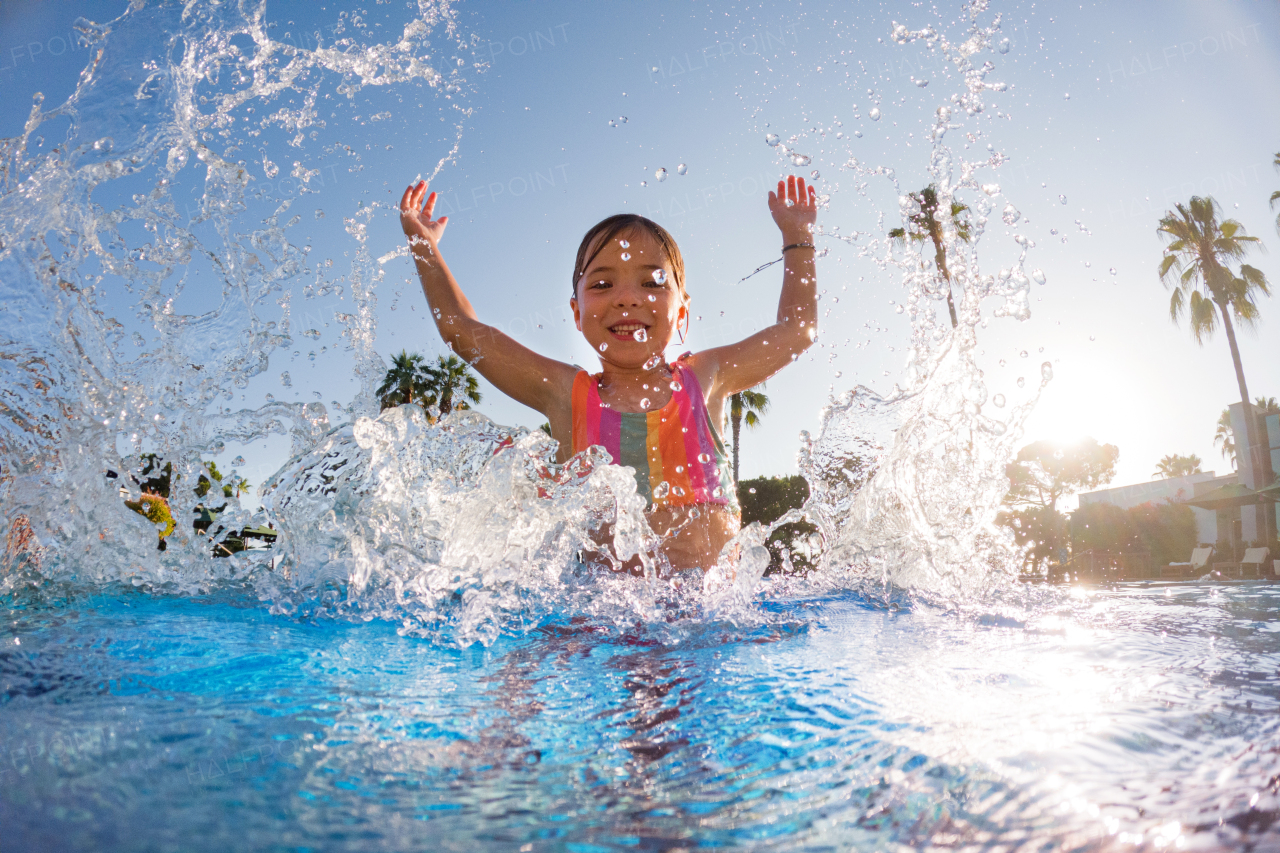 Little girl splashing water in the pool, playing in the water and having fun. Beach resort vacation by the sea. Winter or summer seaside resort holiday.