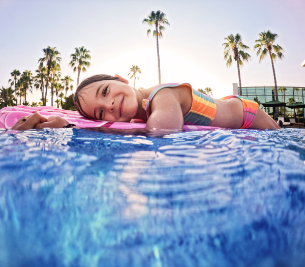 Adorable girl floats on a pink inflatable in the pool. Beach resort vacation by the sea. Winter and summer seaside resort holidays. Over-under underwater photography.