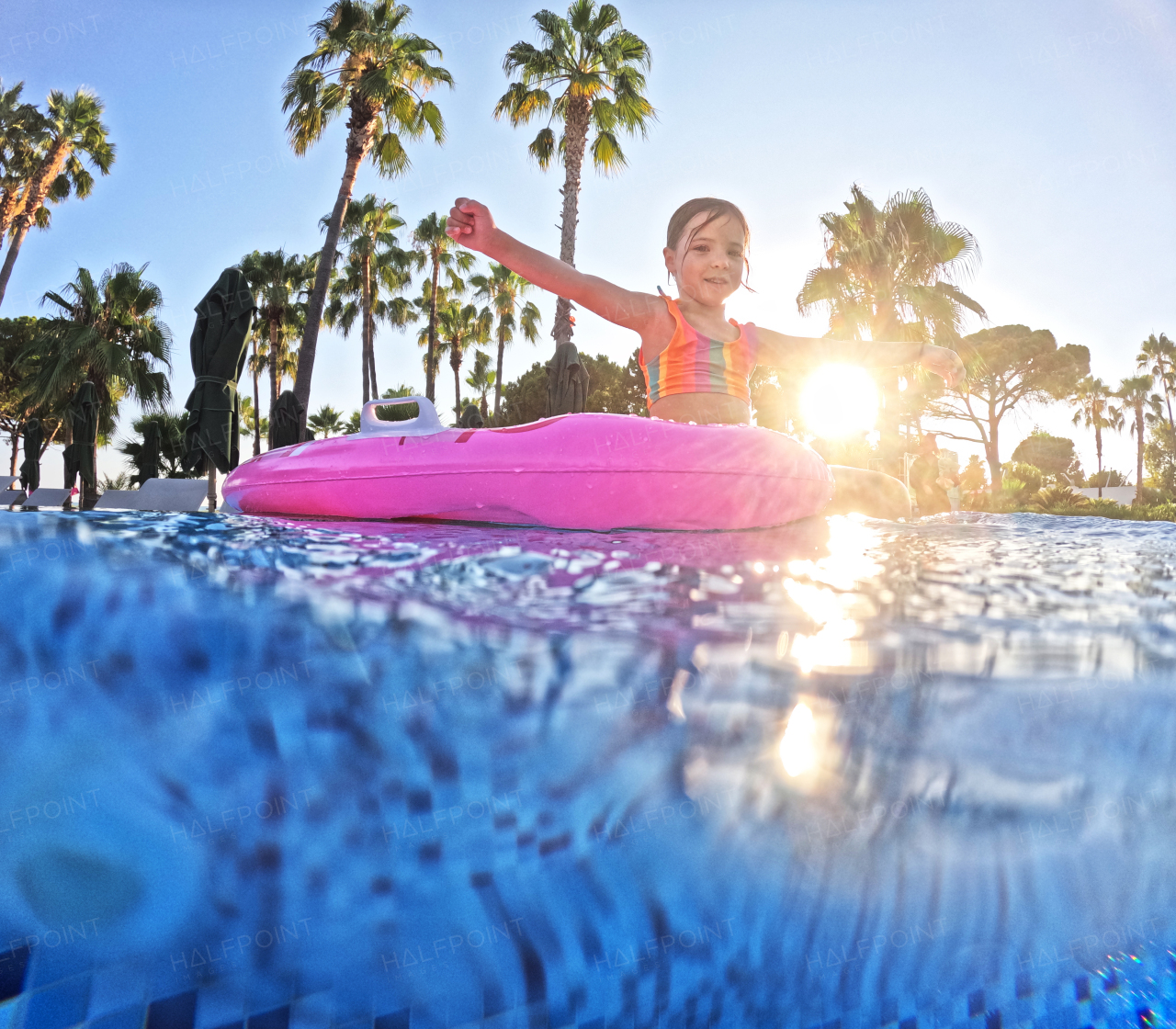 Adorable girl floats on a pink inflatable in the pool. Beach resort vacation by the sea. Winter and summer seaside resort holidays. Over-under underwater photography.