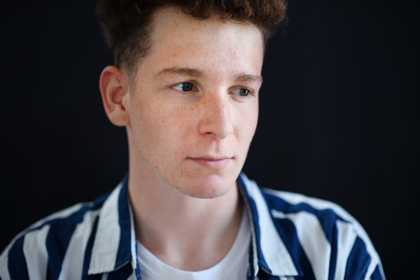 A portrait of thoughtful handsome young man with ginger hair and freckles looking away on black background, close-up