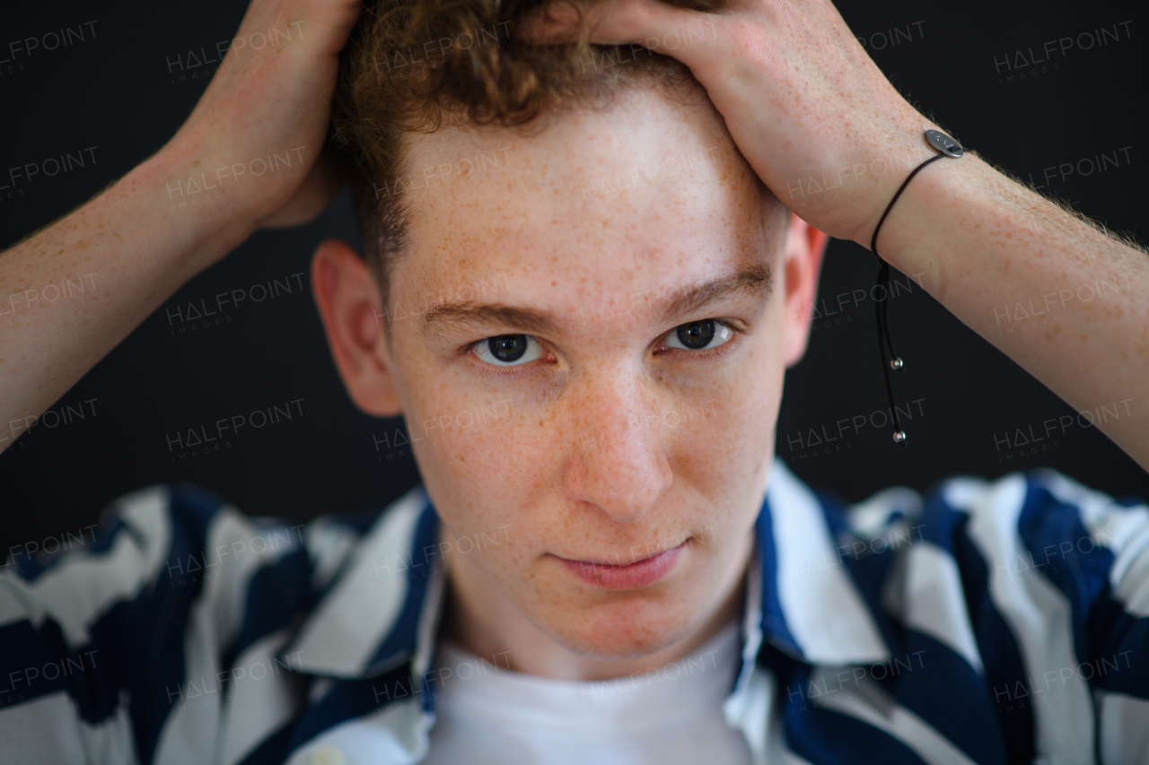 A portrait of thoughtful handsome young man with ginger hair and freckles looking away on black background, close-up