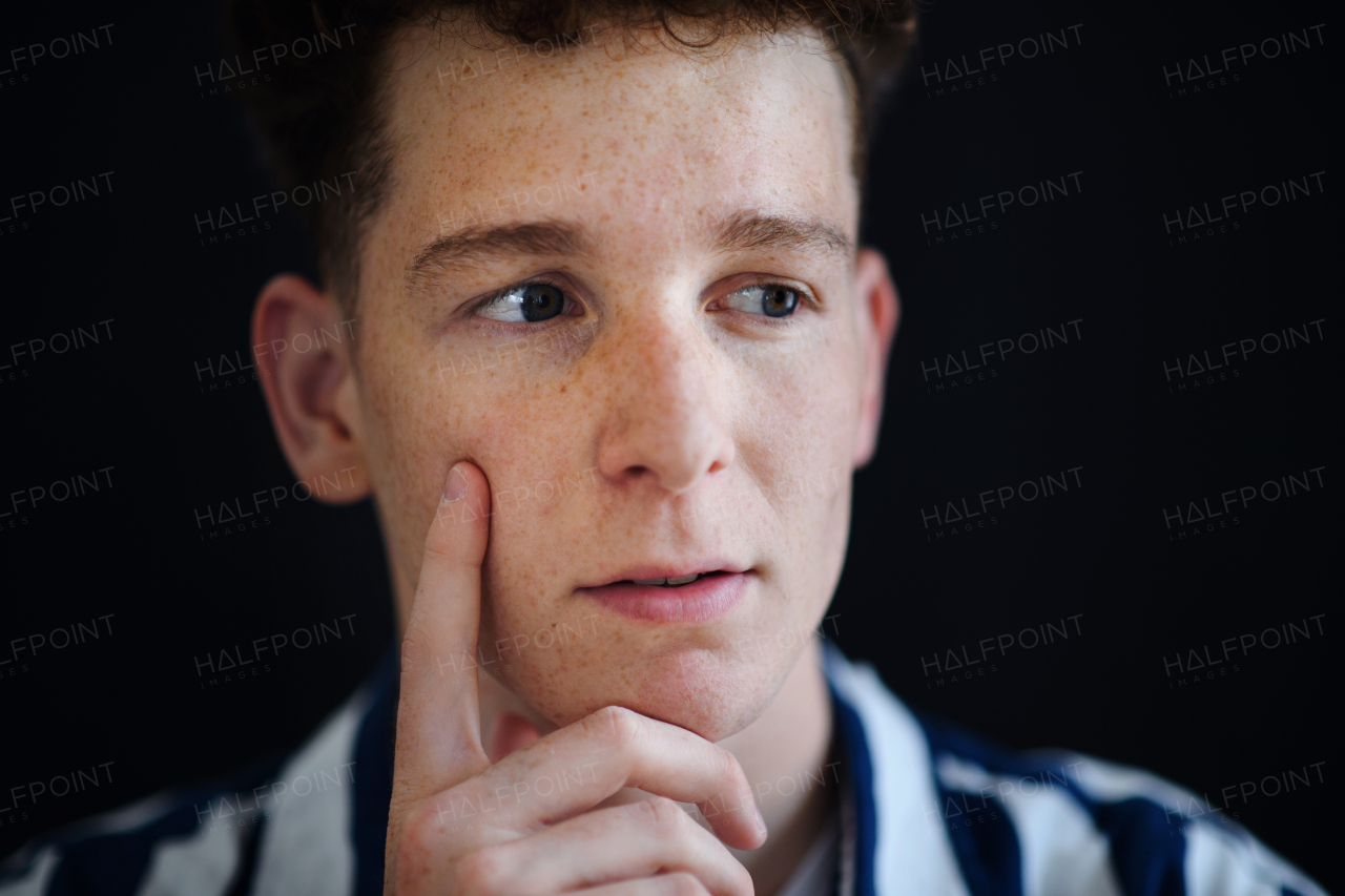 A portrait of thoughtful handsome young man with ginger hair and freckles looking away on black background, close-up