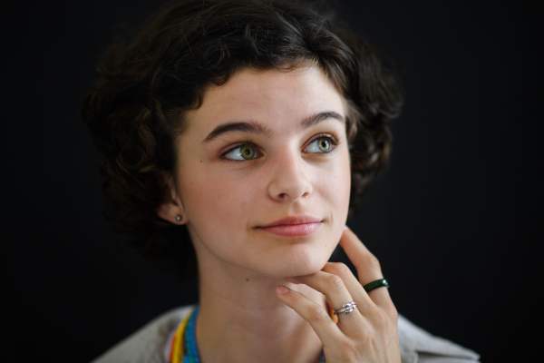 A portrait of confident beautiful teenage girl looking away and daydreaming on black background, close-up