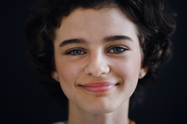 Portrait of a confident beautiful teenage girl looking at camera, on black background, close-up