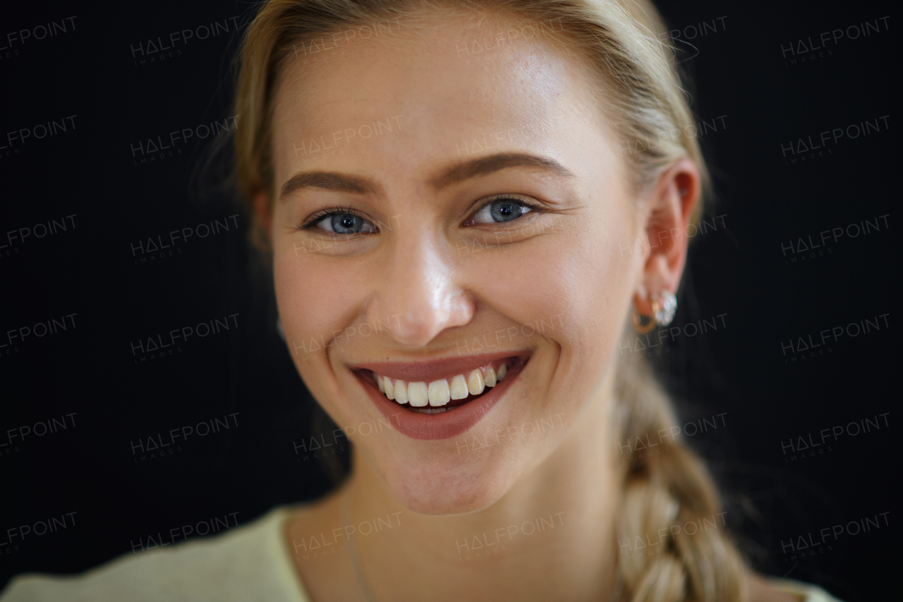 A portrait of beautiful blond young woman looking at camera and smiling on black background, close-up