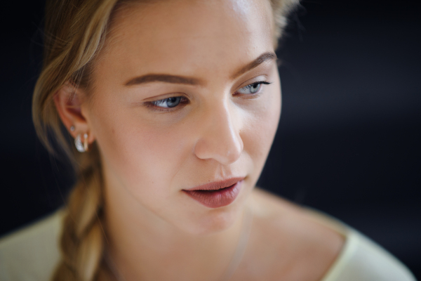 A portrait of beautiful blond young woman looking away and daydreaming on black background, close-up