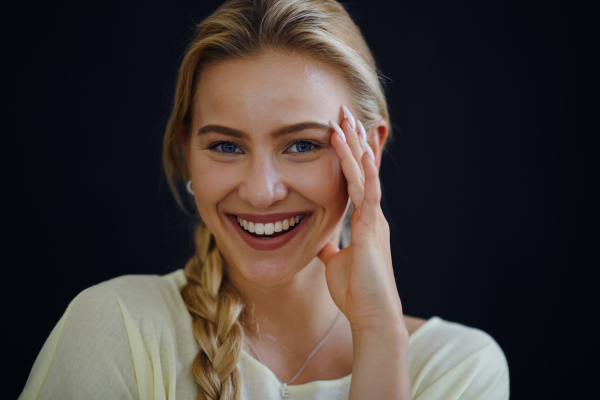 A portrait of beautiful blond young woman looking at camera and smiling on black background, close-up