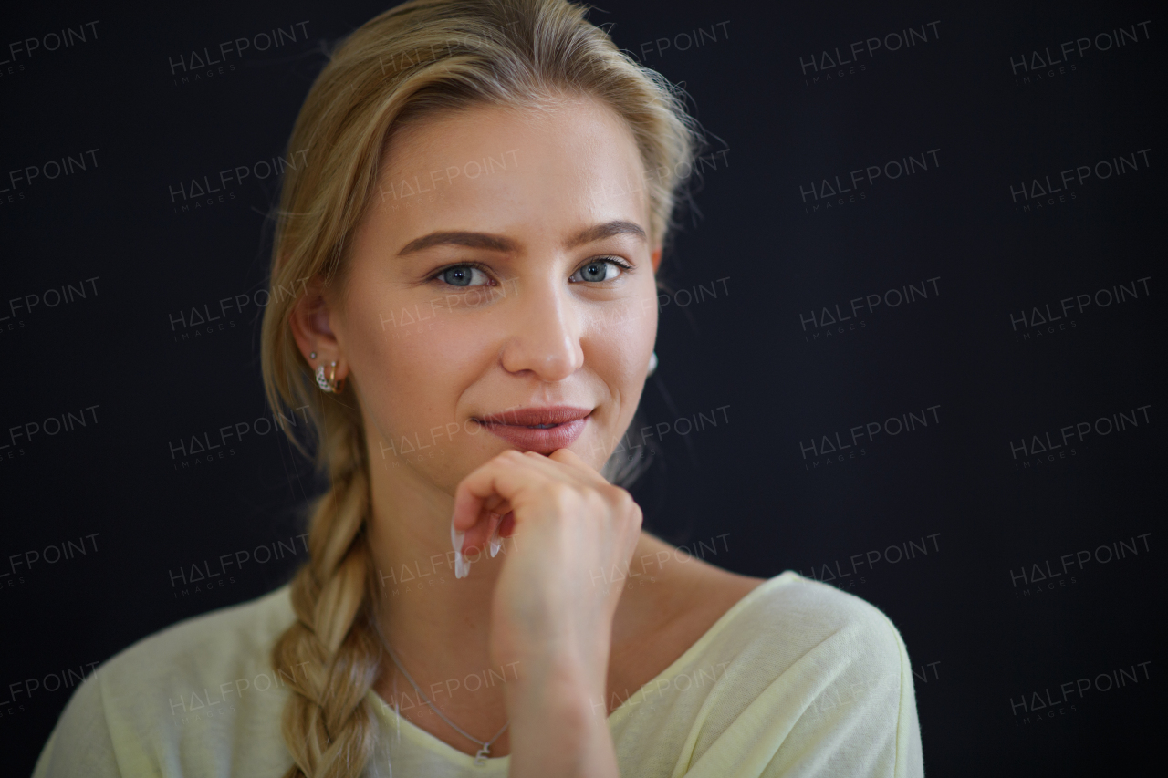 A portrait of beautiful blond young woman looking at camera and smiling on black background, close-up