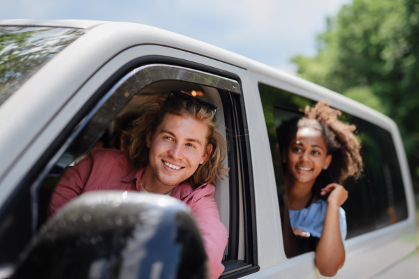 Multiracial young friends travelling together by car, looking through the window and smiling - summer vacation, holidays, travel, road trip and people concept.