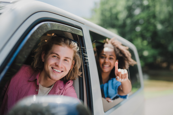 Multiracial young friends travelling together by car, looking through the window and smiling - summer vacation, holidays, travel, road trip and people concept.