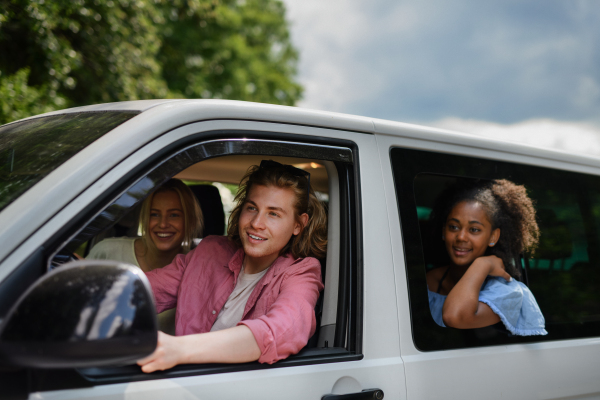 Multiracial young friends travelling together by car, looking through the window and smiling - summer vacation, holidays, travel, road trip and people concept.