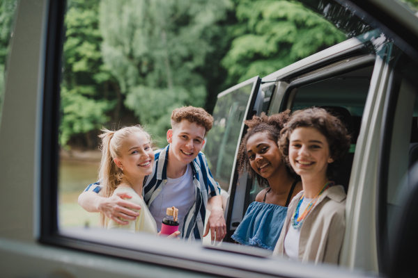 Multiracial young friends travelling together by car, looking through the window and smiling - summer vacation, holidays, travel, road trip and people concept.